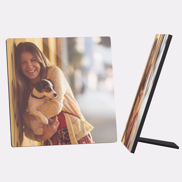 Ein quadratischer Fotoaufsteller zeigt ein fröhliches Bild von einer jungen Frau, die einen kleinen Hund im Arm hält.